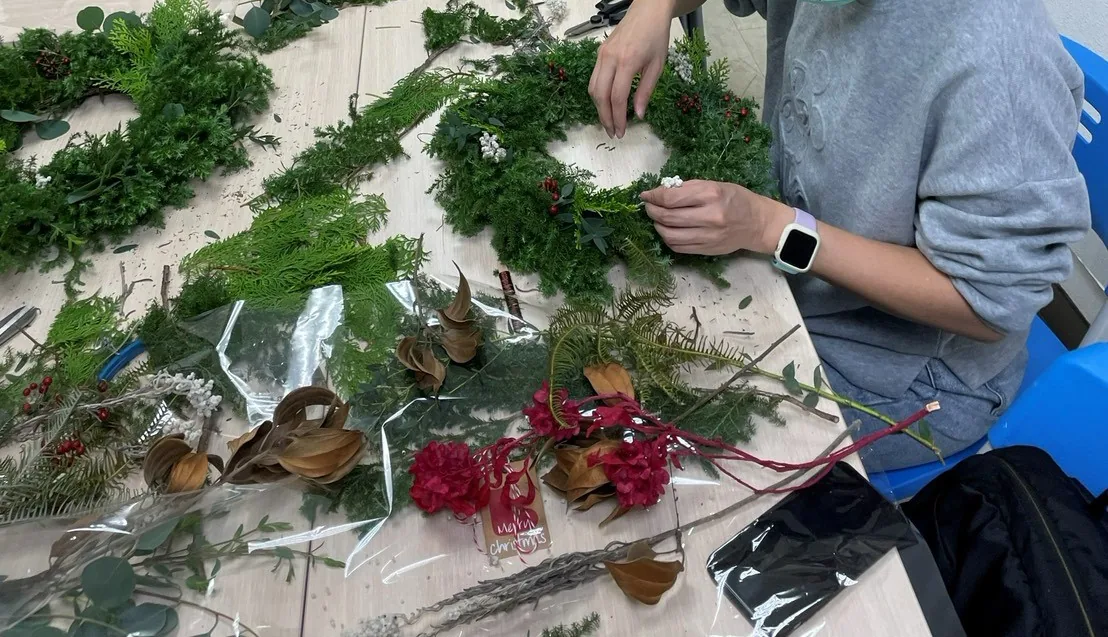 學員在長桌上以雪松與紅色花材製作聖誕花圈